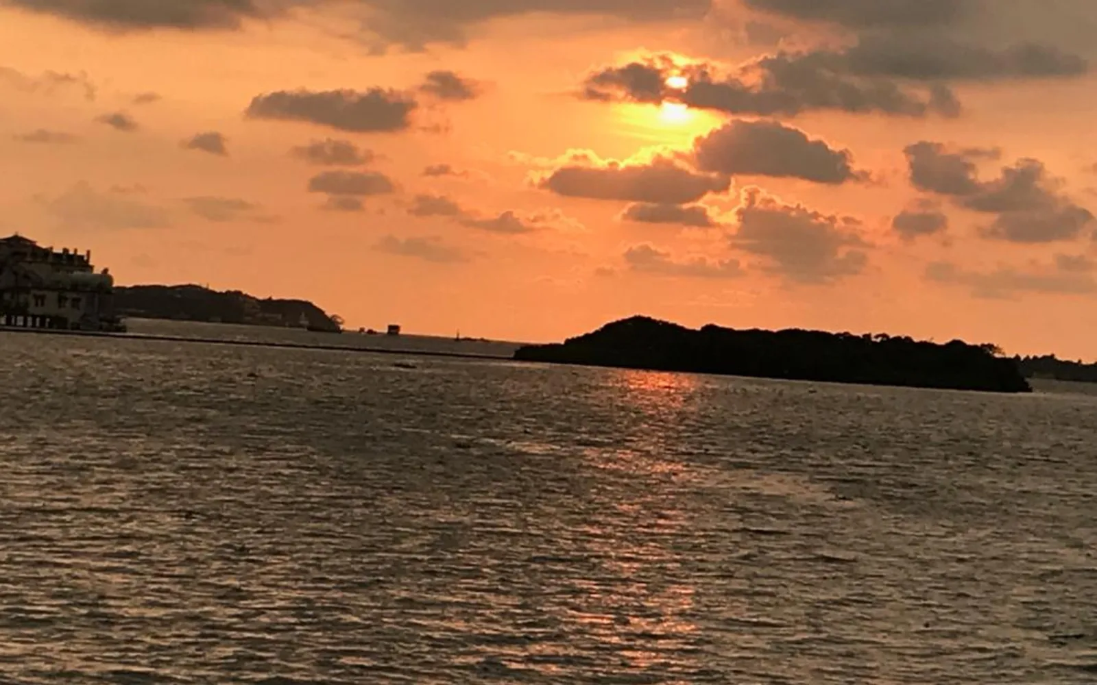 A lake view at sunset with the sun partially obscured by clouds